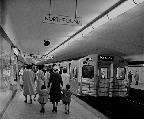 Subway train in with destination EGLINTON sits in glossy-tiled station. Signs in black type on white read NORTHBOUND, &larr; STREET CARS ONLY, NOT TO BLOOR STREET